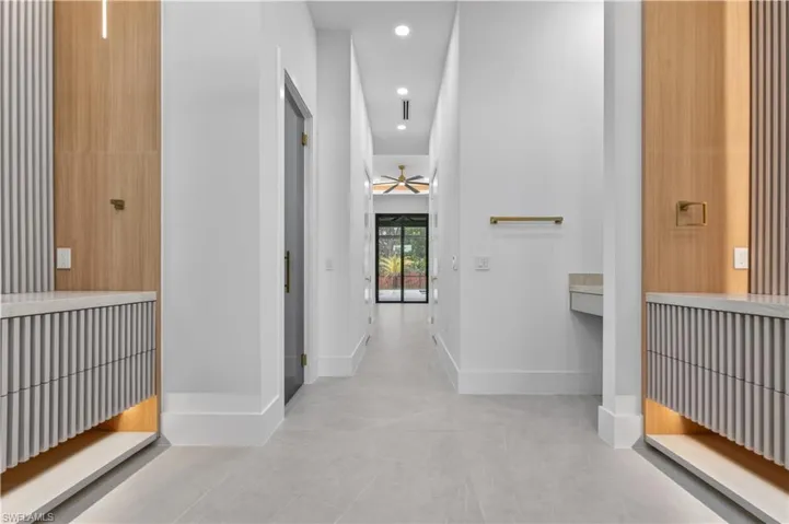 Spacious corridor featuring light wood-finish wall panels, integrated linear lighting, and built-in fluted cabinetry with undermount illumination