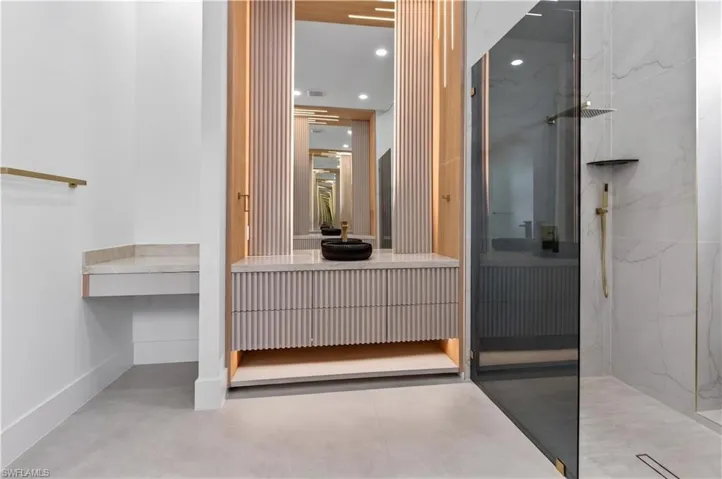 Modern bathroom featuring a fluted vanity with a vessel sink, integrated lighting, and a large mirror