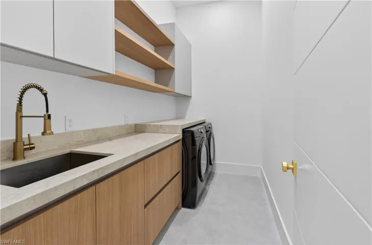 Laundry area featuring light wood-finish cabinetry, light-colored countertops, and a dark undermount sink with a brass-finish faucet