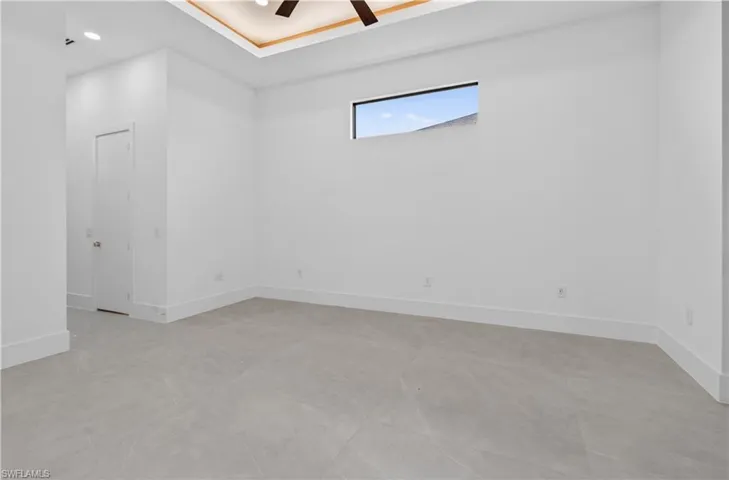 Spacious room featuring light-toned tile flooring, a tray ceiling with recessed lighting, and a modern ceiling fan