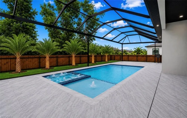 Screened outdoor area featuring a swimming pool with integrated spa and water feature, light-toned patio tile, and a wooden privacy fence with mature palm trees