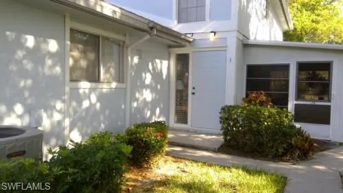 Entryway featuring a solid panel door with a sidelight, an exterior light fixture, and established shrubbery