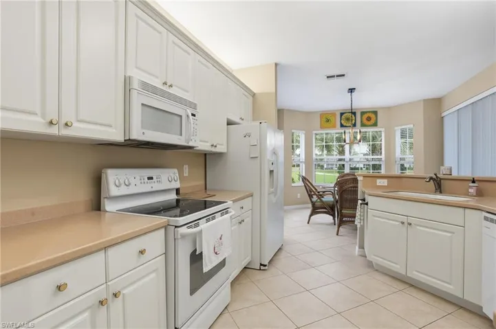 Kitchen with white appliances, white cabinetry, light countertops, light tile patterned floors, and decorative light fixtures