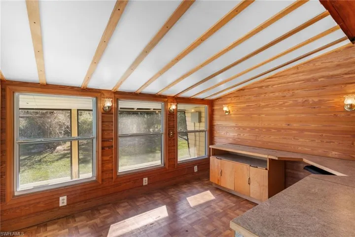 Unfurnished dining area with wood walls, parquet flooring, and lofted ceiling with beams
