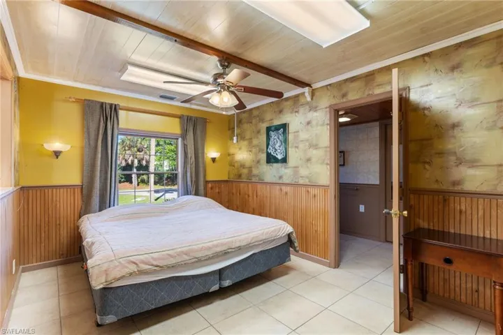 Bedroom featuring wood ceiling, wainscoting, ceiling fan, wooden walls, and crown molding