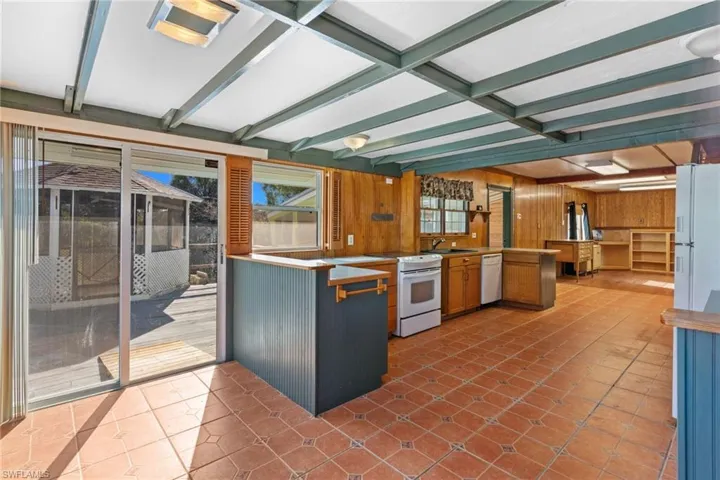Kitchen featuring a peninsula, light tile patterned flooring, white appliances, wooden walls, and wood finish cabinets