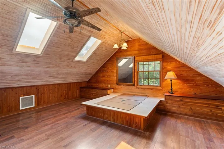 Bonus room with wooden walls, dark wood-type flooring, suspended lighting, a skylight, and a vaulted wooden ceiling