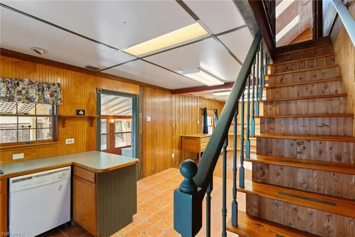 Kitchen with white dishwasher, wooden walls, light countertops, wood finish cabinets, and a peninsula