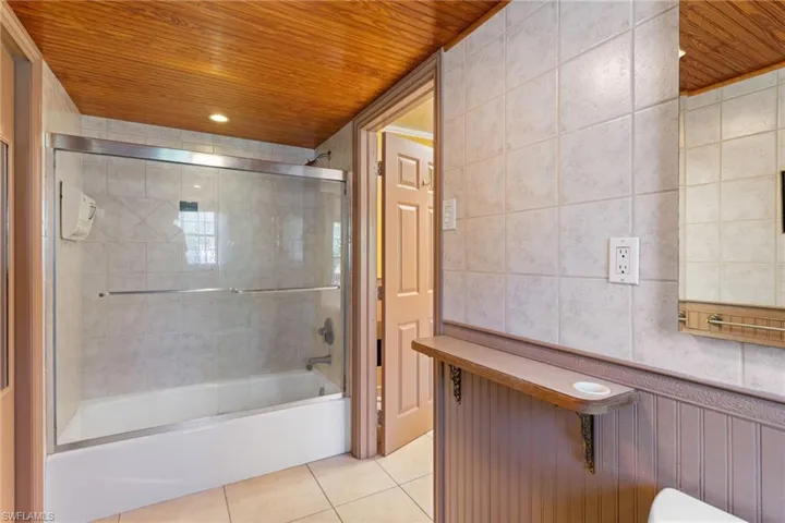 Bathroom with enclosed tub / shower combo, wooden ceiling, light tile patterned floors, and tile walls