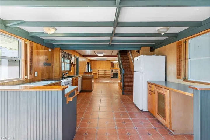 Kitchen with wood walls, white appliances, a peninsula, wood finish cabinetry, and beamed ceiling