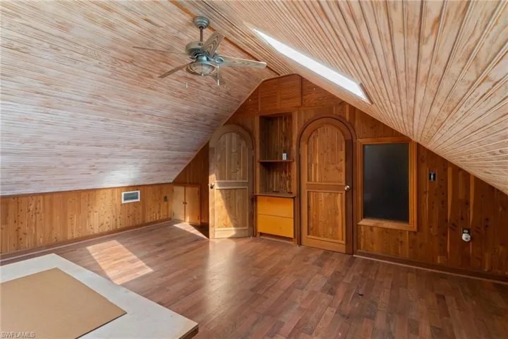 Additional living space featuring wood walls, a skylight, dark wood-style flooring, wood ceiling, and ceiling fan