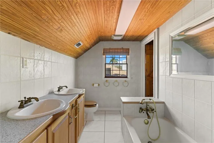 Bathroom with tile walls, double vanity, a bath, and a vaulted wood ceiling