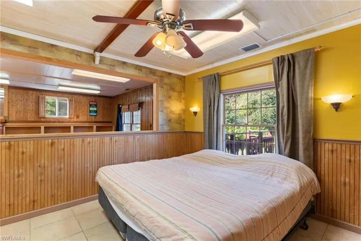Bedroom with wooden walls, multiple windows, wainscoting, wooden ceiling, and access to outside
