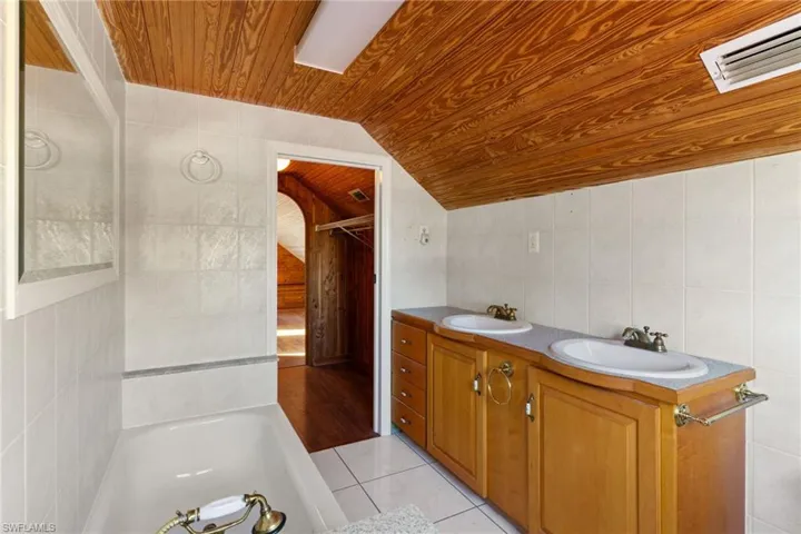 Bathroom featuring tile walls, double vanity, a bath, light tile patterned flooring, and a vaulted wooden ceiling