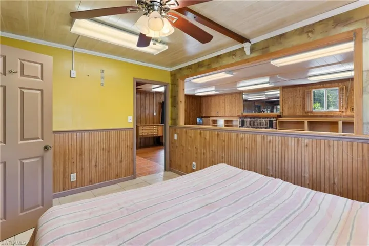 Bedroom with wooden walls, a wainscoted wall, light tile patterned floors, and wooden ceiling