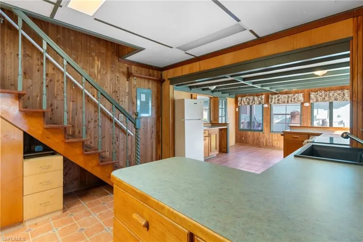 Kitchen with wooden walls, freestanding refrigerator, light tile patterned floors, wood finish cabinetry, and light countertops