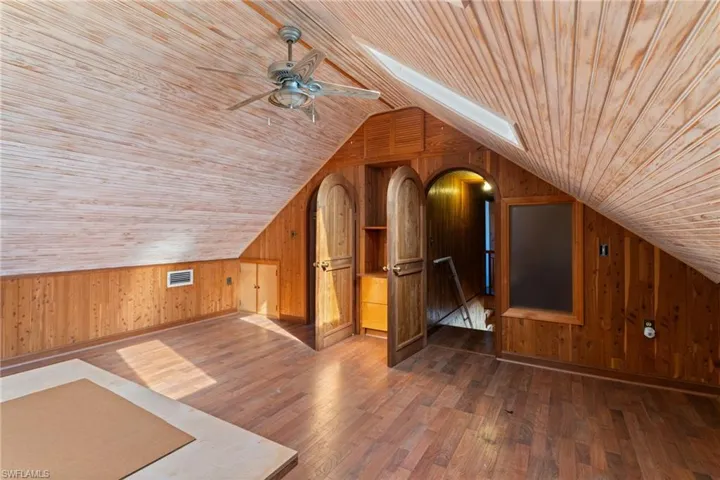 Additional living space featuring wooden walls, a skylight, dark wood-style floors, wood ceiling, and a ceiling fan
