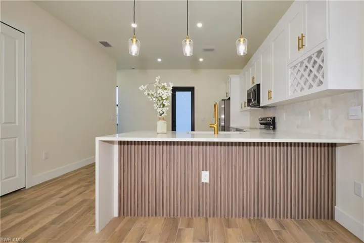 Kitchen with white cabinets, a peninsula, light stone counters, and light wood-type flooring