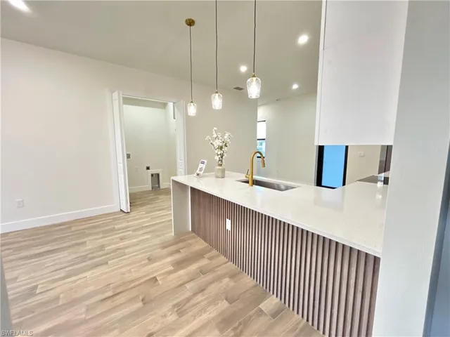 Kitchen featuring light stone countertops, recessed lighting, light wood-style flooring, pendant lighting, and a peninsula