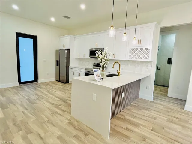 Kitchen with a peninsula, appliances with stainless steel finishes, light stone countertops, white cabinetry, and hanging light fixtures