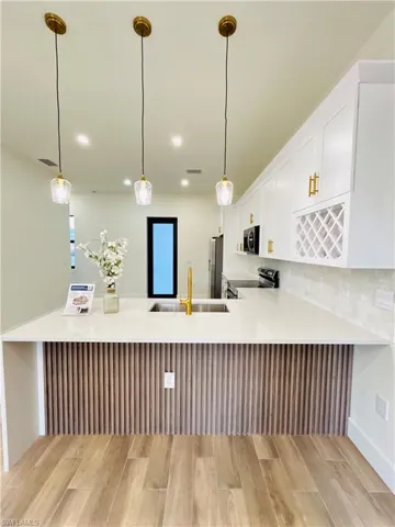 Kitchen featuring a peninsula, white cabinets, hanging light fixtures, stainless steel appliances, and a breakfast bar