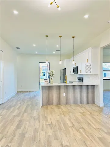 Kitchen with light wood finished floors, white cabinetry, a peninsula, pendant lighting, and recessed lighting