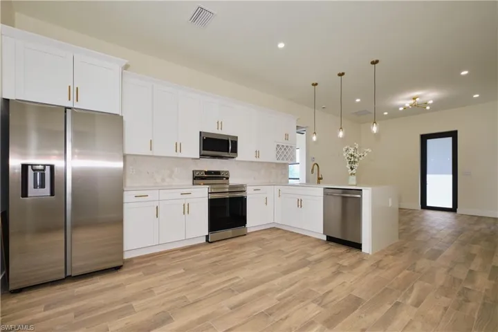 Kitchen featuring appliances with stainless steel finishes, white cabinetry, pendant lighting, recessed lighting, and tasteful backsplash