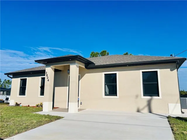 View of front of home with a shingled roof, stucco siding, and a front lawn