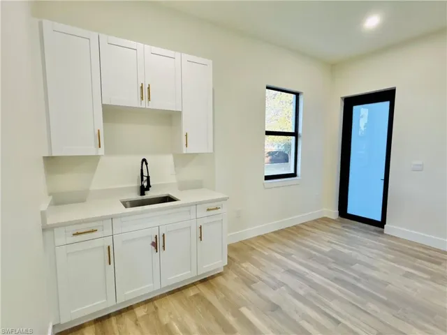 Kitchen with white cabinetry, light stone countertops, and light wood-type flooring