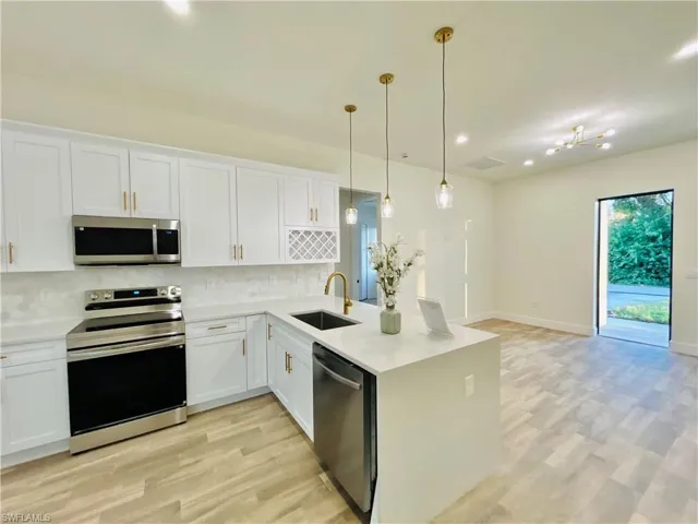 Kitchen with appliances with stainless steel finishes, a peninsula, white cabinets, decorative light fixtures, and recessed lighting