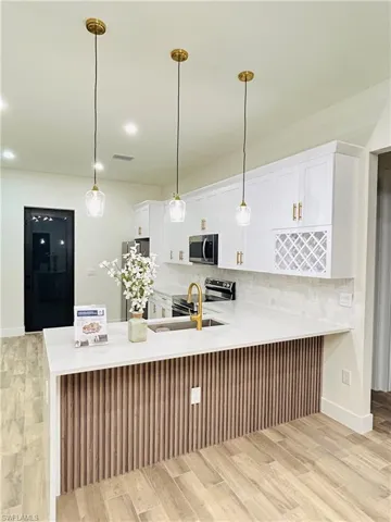 Kitchen featuring light wood-style floors, pendant lighting, white cabinetry, stainless steel appliances, and a peninsula
