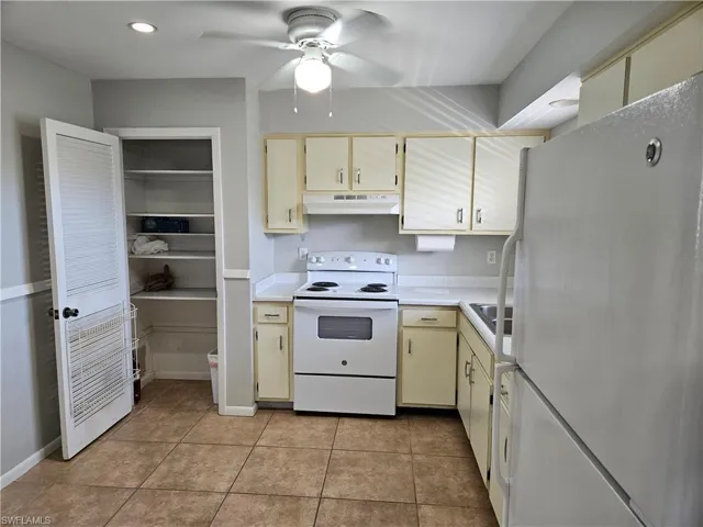 Kitchen with ceiling fan, cream cabinets, light tile patterned floors, and white appliances