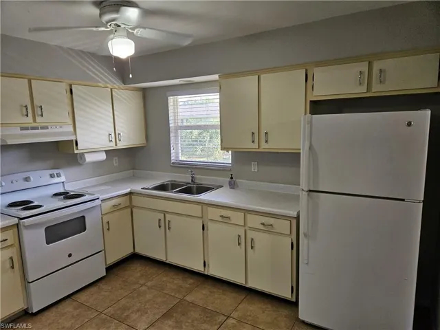 Kitchen with white appliances, ceiling fan, sink, light tile patterned floors, and cream cabinetry