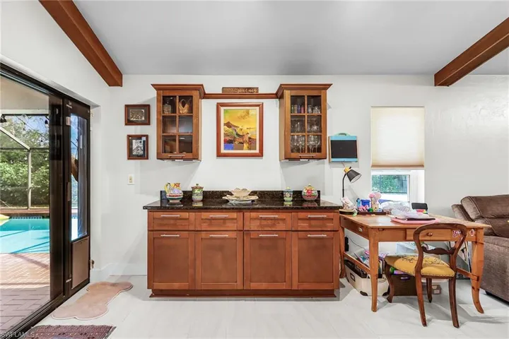 Bar featuring beam ceiling, dark stone countertops, glass fronted cabinets, and healthy amount of natural light