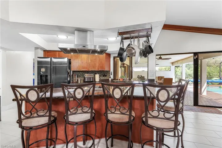 Kitchen featuring wood finish cabinetry, island exhaust hood, fridge with ice dispenser, light tile patterned flooring, and a breakfast bar