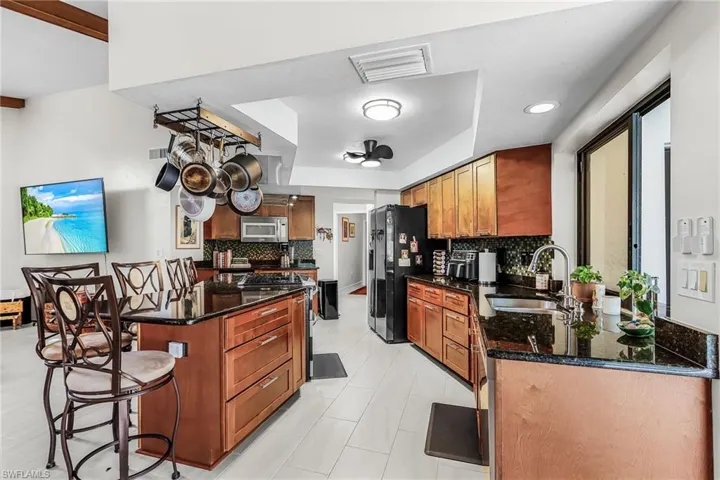 Kitchen with a kitchen bar, dark stone countertops, wood finish cabinets, stainless steel appliances, and backsplash
