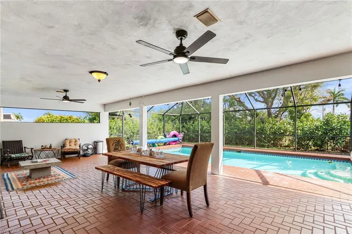 Outdoor pool with glass enclosure, a patio area, an outdoor living space with a fire pit, and a sunroom
