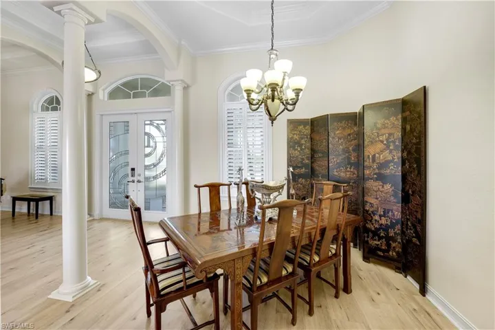Dining area with ornate columns, light wood-type flooring, arched walkways, french doors, and suspended lighting