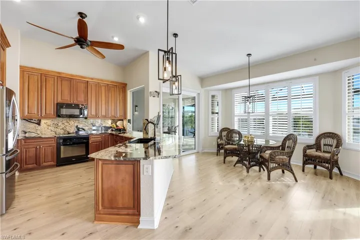 Kitchen with wood finish cabinetry, light stone counters, black appliances, a chandelier, and backsplash