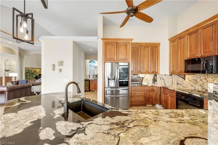 Kitchen with a ceiling fan, light stone counters, black appliances, wood finish cabinetry, and arched walkways