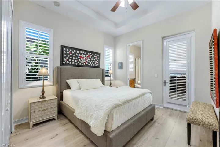 Bedroom with light wood finished floors, ceiling fan, multiple windows, and a raised ceiling
