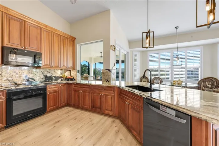 Kitchen with black appliances, light wood-style flooring, light stone countertops, and wood finish cabinetry
