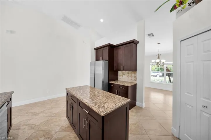 Kitchen with freestanding refrigerator, a chandelier, dark brown cabinetry, decorative backsplash, and light stone counters