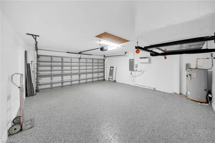 Garage featuring water heater, a garage door opener, electric panel, and a wall mounted air conditioner