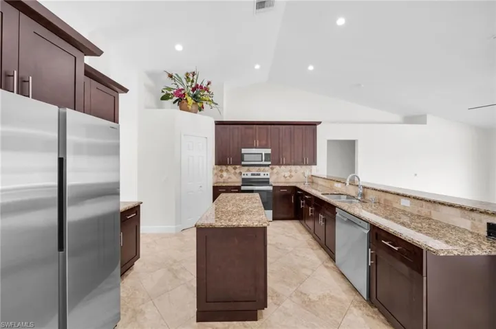 Kitchen featuring appliances with stainless steel finishes, backsplash, a peninsula, a center island, and light stone countertops