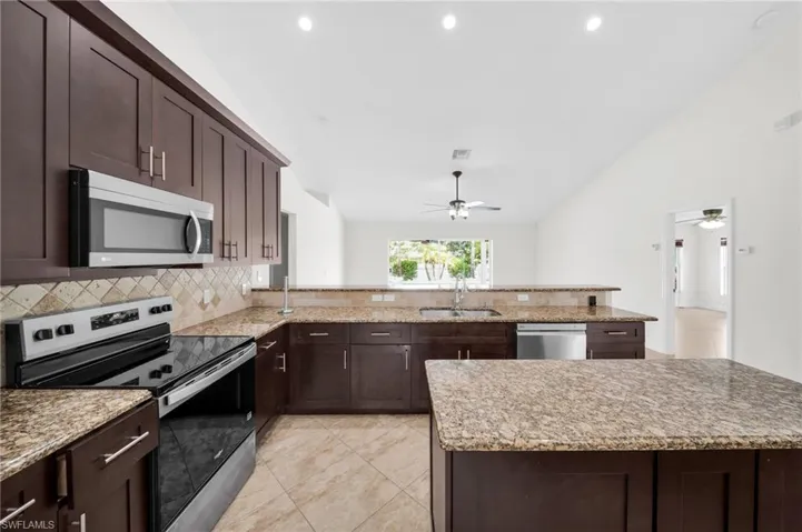 Kitchen with stainless steel appliances, a ceiling fan, decorative backsplash, lofted ceiling, and dark brown cabinets
