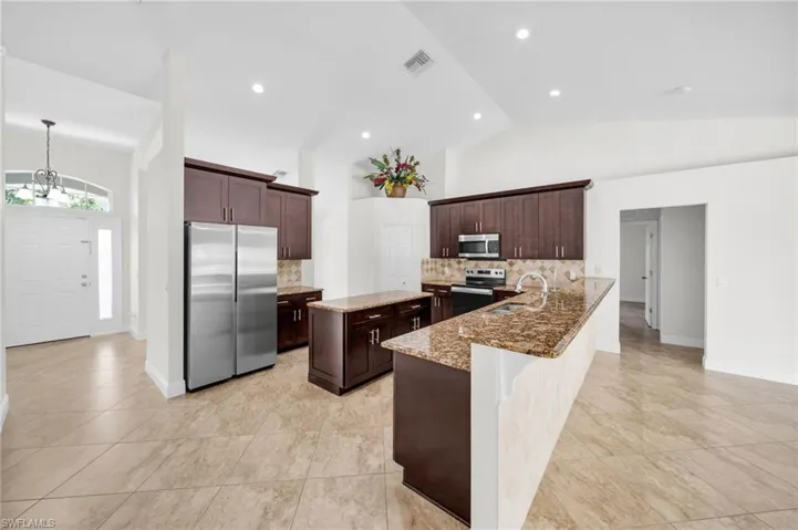 Kitchen featuring ' appliances with stainless steel finishes, decorative backsplash, a chandelier, light stone countertops, and dark brown cabinets