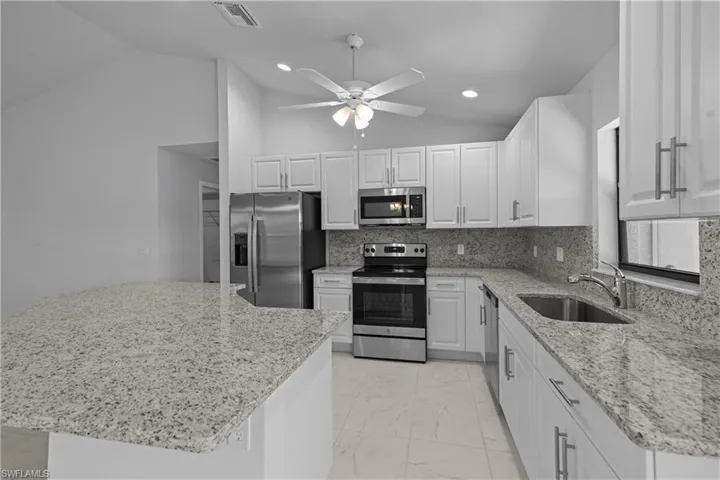 Kitchen with stainless steel appliances, vaulted ceiling, a kitchen island, light stone countertops, and ceiling fan