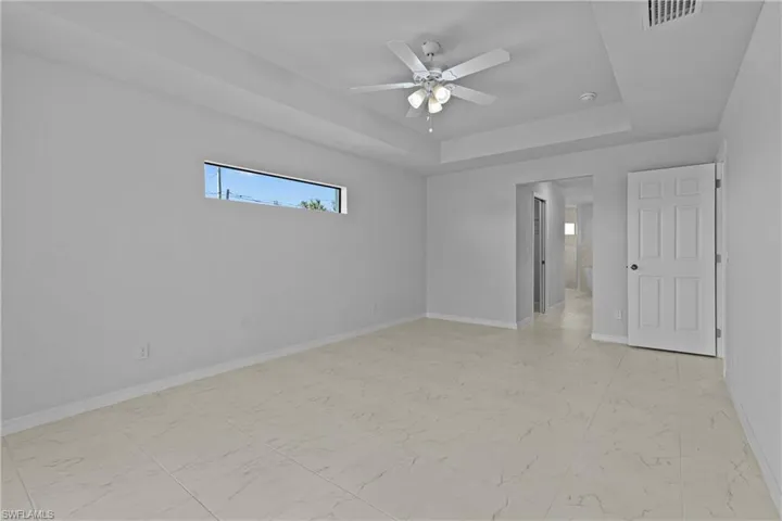 Unfurnished bedroom with connected bathroom, light marble finish flooring, a ceiling fan, and a raised ceiling