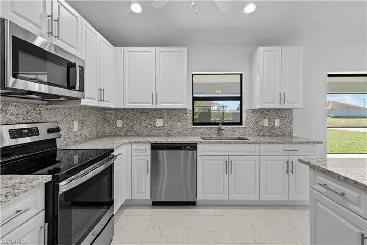 Kitchen with stainless steel appliances, white cabinets, light marble finish floors, light stone countertops, and recessed lighting